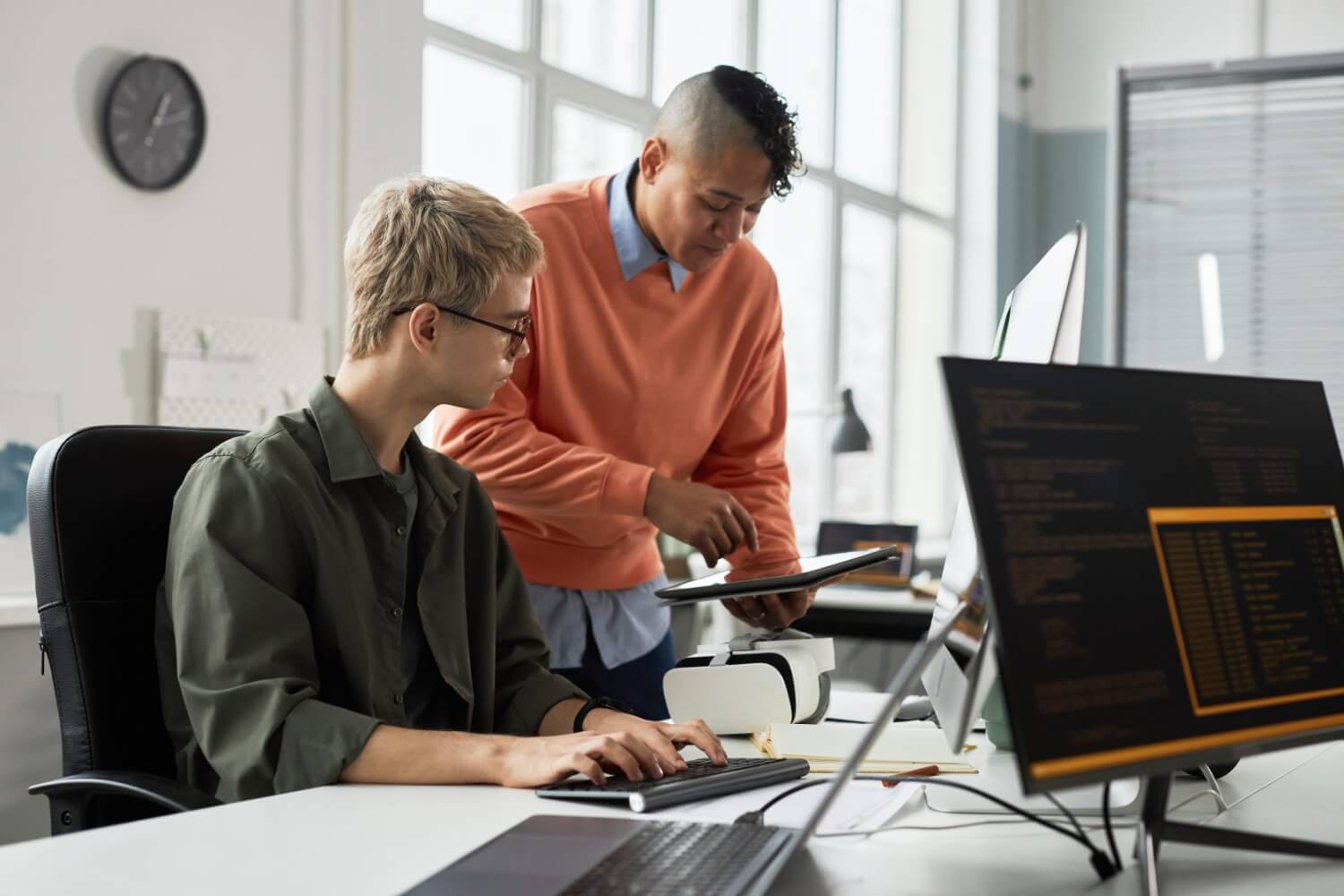 Two men looking at a tablet with a computer in the background